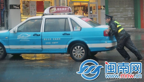 一名協(xié)警奮力推車，幫助的哥將車輛移走