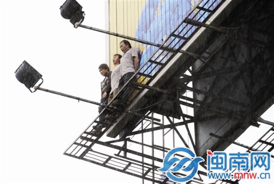 大雨中，幾名工人緊貼廣告牌，但渾身已被淋濕