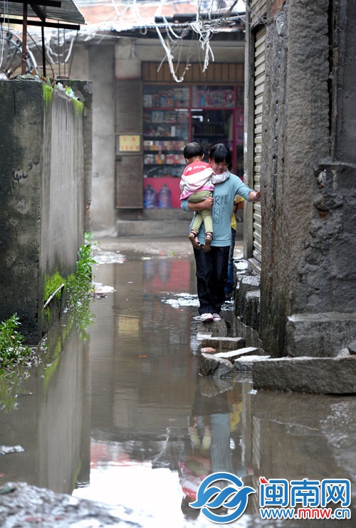 一位媽媽抱著孩子，小心翼翼踏著石塊，穿過積水路段